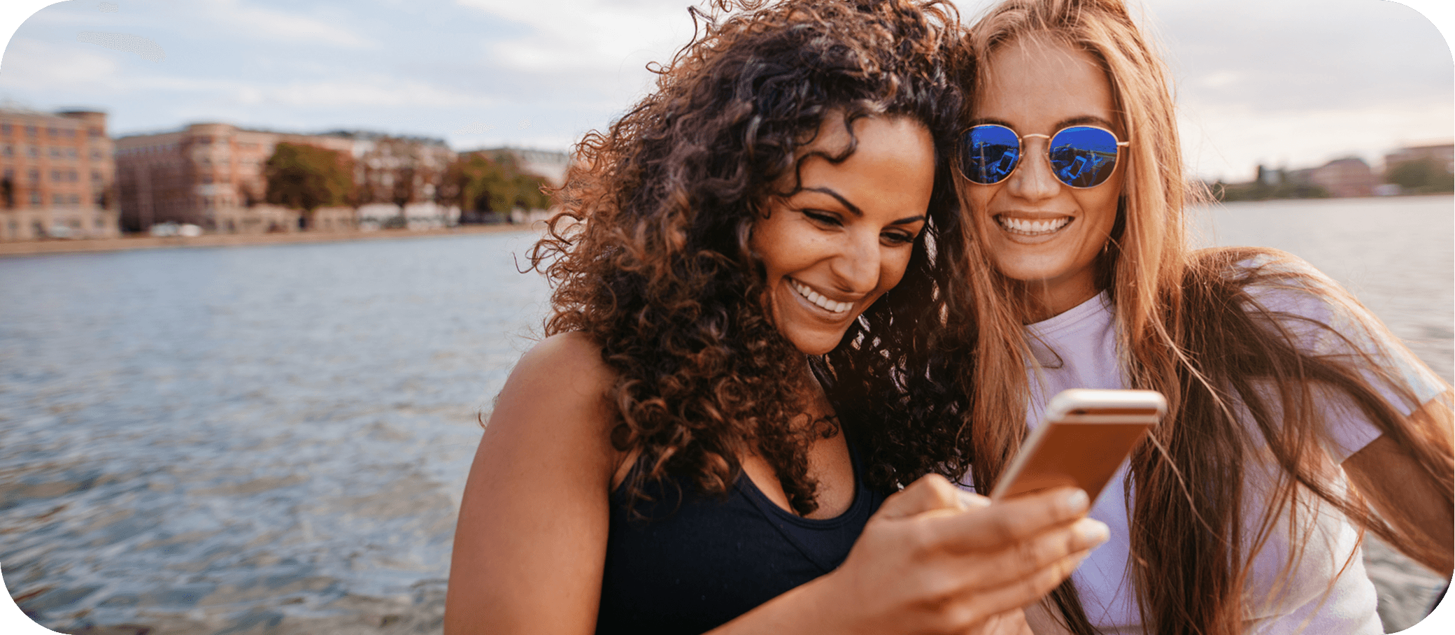 Two friends smiling at a phone together by the water